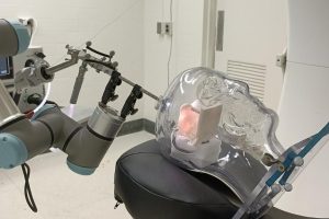 Image of robotic arm targeting a specific section of a clear plastic human skull laying on a table