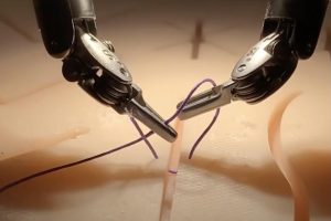 Two surgical robot arms hold and tie suture material in a simulated surgical setting