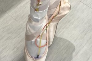 Photo of someone wearing ballet shoes and the PointeSense system, which consists of red and yellow wires running from the wearer&#039;s toes to their ankles