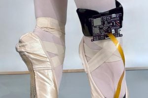 Close-up image of a dancer standing on her toes in ballet pointe shoes; a black control board is wrapped around her right ankle and connected into the toe of the shoe