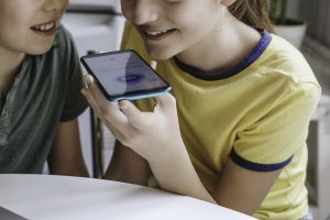 Two children speak to a chatbot on a cellphone.