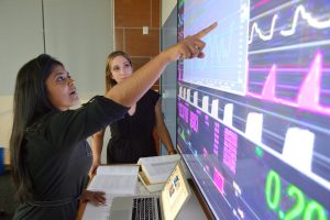 Two people looks at figures and graphs on a large computer screen